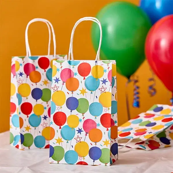 Colourful party gift bags with balloon prints displayed alongside bright balloons and matching party accessories.